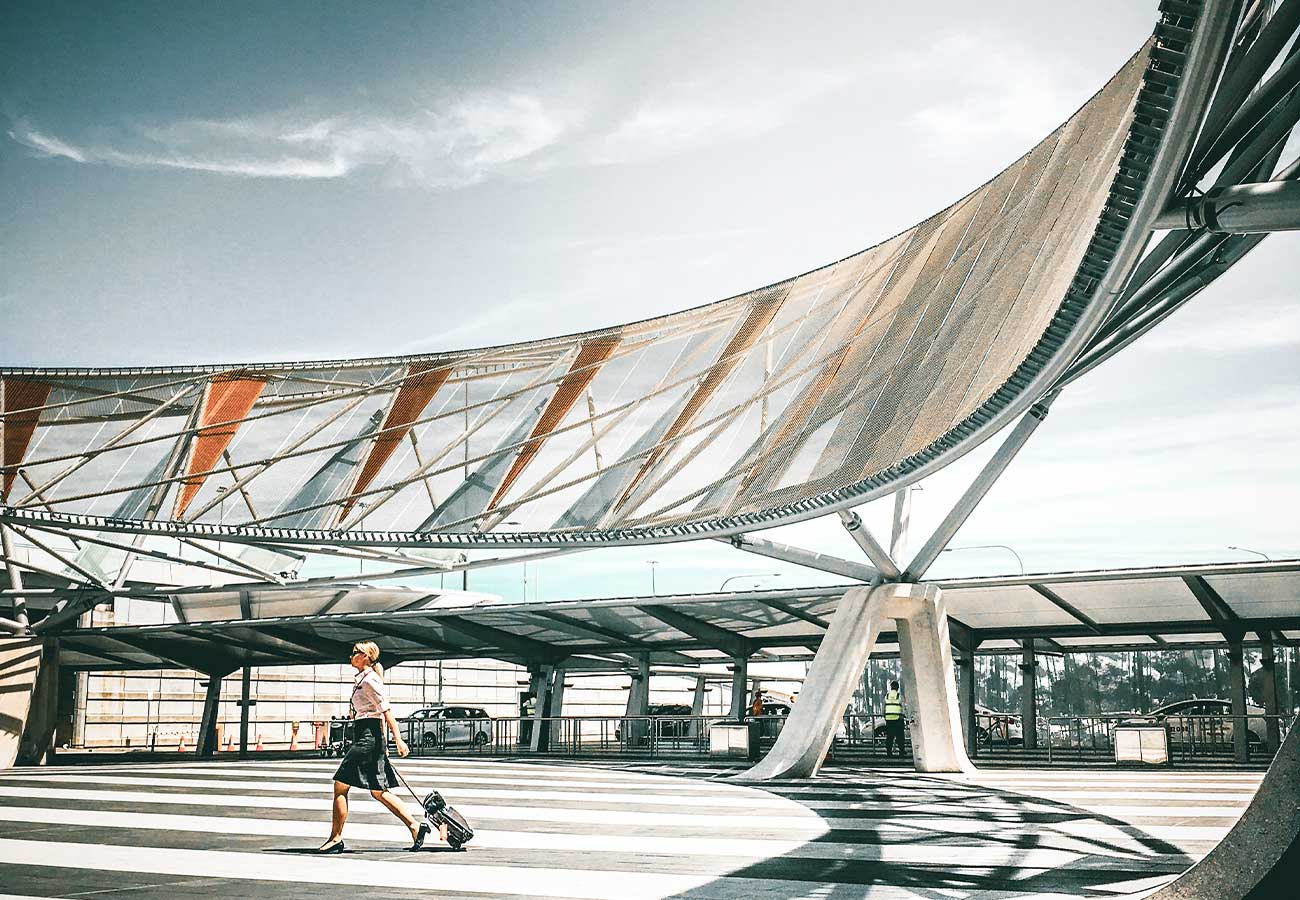 Woman jogging with luggage under modern curved architectural structure with glass and metal canopy