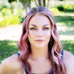 Woman with long wavy purple-pink hair smiling outdoors in natural sunlight